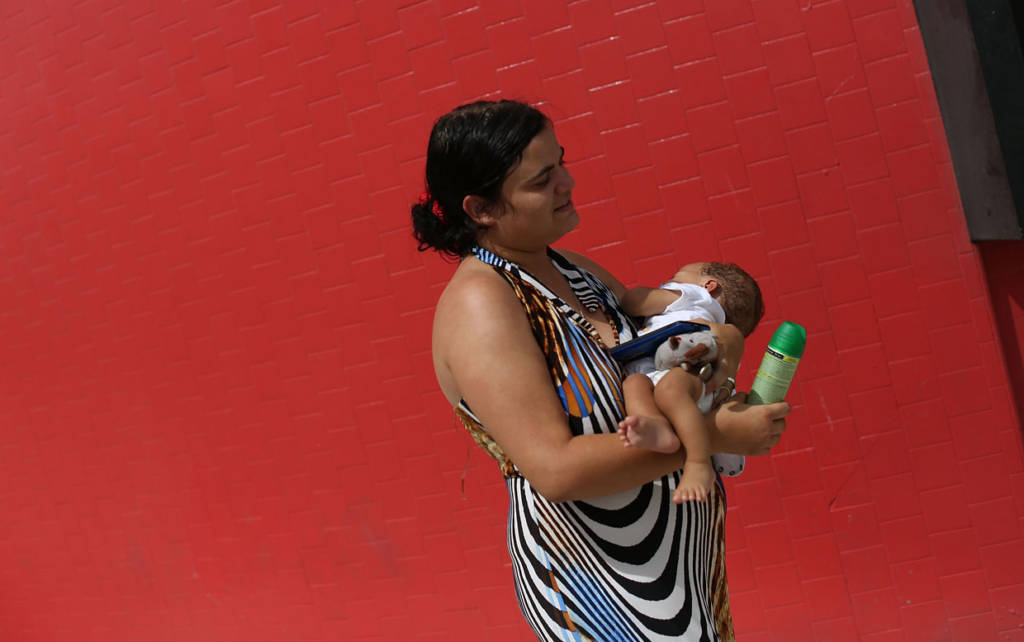 MIAMI, FL - AUGUST 02: Barbara Betancourt holds her baby Daniel Valdes after being given a can of insect repellent by James Bernat, a City of Miami police officer, as he helps people living around the Miami Rescue Mission prevent mosquito bites that may infect them with the Zika virus on August 2, 2016 in Miami, Florida. A reported 14 individuals have been infected with the Zika virus by local mosquitoes. (Photo by Joe Raedle/Getty Images)