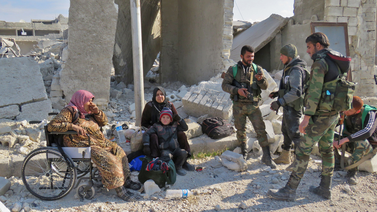 Syrian pro-government forces stand next to residents of Aleppo's Sheikh Saeed district, on December 12, 2016, after troops retook the area from rebel fighters. / AFP / STRINGER (Photo credit should read STRINGER/AFP/Getty Images)