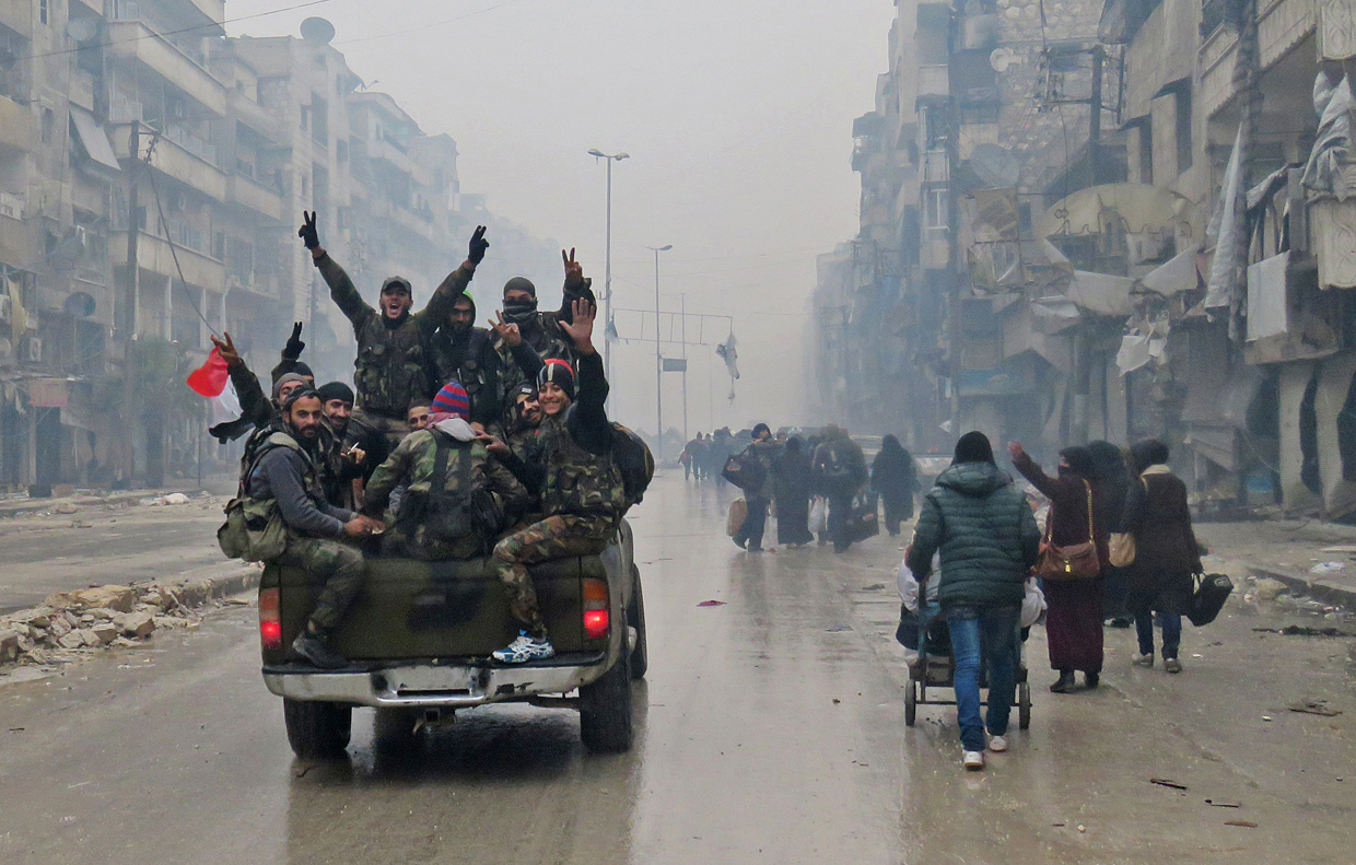 TOPSHOT - Syrian pro-regime fighters, gesture as they drive past residents fleeing violence in the restive Bustan al-Qasr neighbourhood, in Aleppo's Fardos neighbourhood on December 13, 2016, after regime troops retook the area from rebel fighters. Syrian rebels withdrew from six more neighbourhoods in their one-time bastion of east Aleppo in the face of advancing government troops, the Syrian Observatory for Human Rights said. / AFP / STRINGER (Photo credit should read STRINGER/AFP/Getty Images)