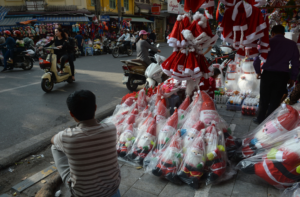 This photo taken on December 21, 2016 shows a vendor (L) sitting next to his stand selling Christmas items in downtown Hanoi. / AFP / HOANG DINH NAM (Photo credit should read HOANG DINH NAM/AFP/Getty Images)