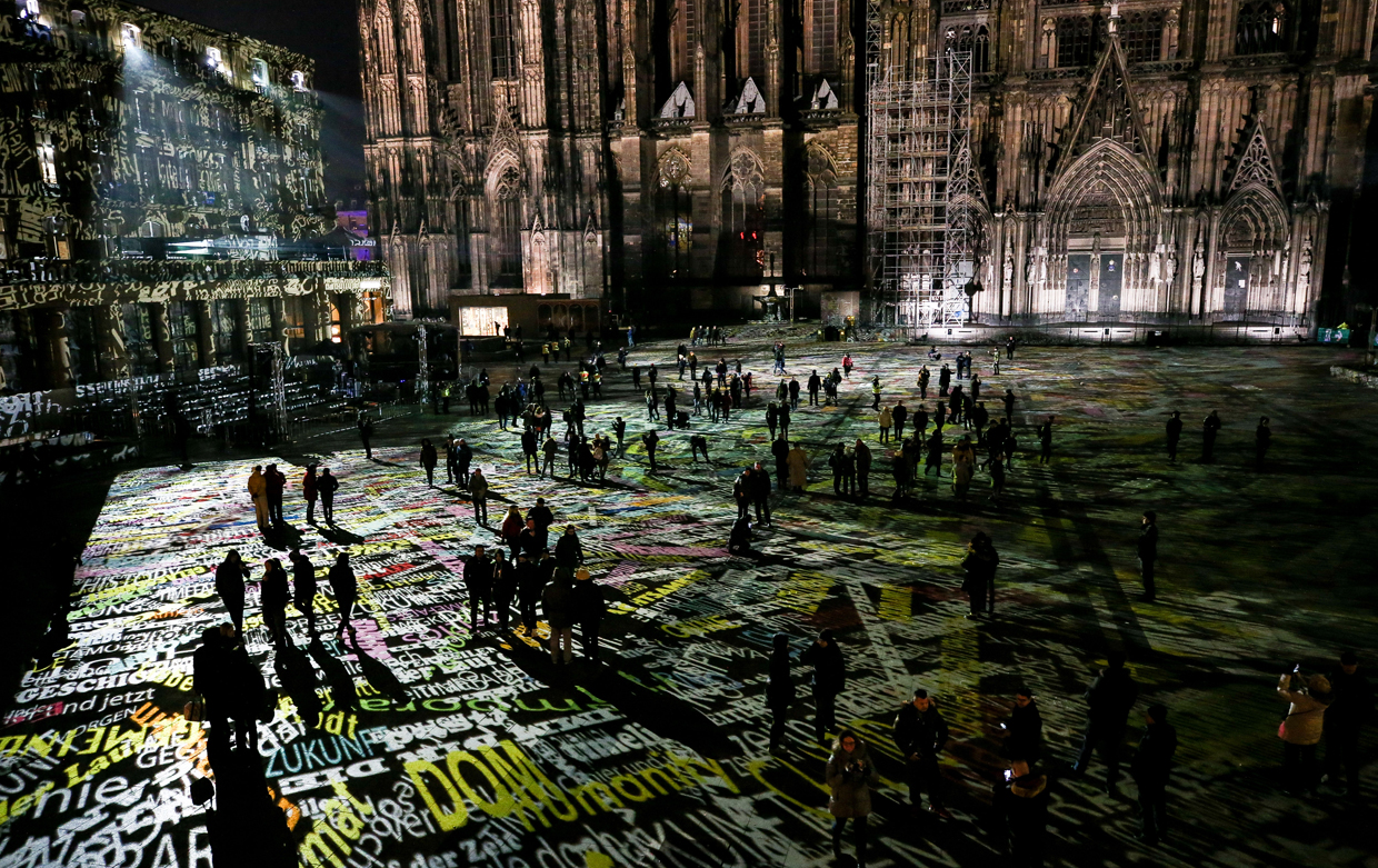 COLOGNE, GERMANY - DECEMBER 31: Visitors are seen as words are being projected onto the ground and the walls of the surrounding buildings in front of the Cologne Cathedral during the light installation by the artist Philipp Geist in Cologne, where on New Year's Eve one year ago hundreds of apparently coordinated sexual assaults were perpetrated against women, prior to New Year's Eve celebrations on December 31, 2016 in Cologne, Germany. City authorities have deployed around 1,500 police officers - more than 10 times last year's number, to maintain security during this year's festivities. Security across Germany is high due also to the recent Berlin terror attack, in which suspect Anis Amri drove a truck into a Christmas market and killed 12 people. (Photo by Maja Hitij/Getty Images)