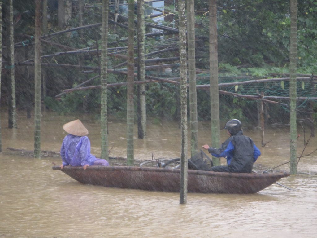 Một phụ nữ đang được chở giúp về nhà vì đường vào nhà chị đã ngập sâu. (Hình: Liêu Thái/Người Việt)