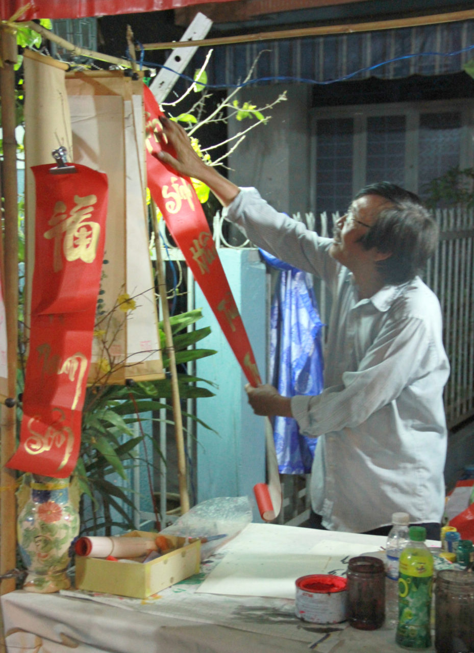 Ông đồ Ðỗ Tường Chinh sung sướng mãn nguyện ngắm đôi liễn “Nhân sinh hữu tửu tu đương túy/ Nhất chích hà tàng đáo cửu nguyên” (Lúc sống có rượu cứ nên uống bằng say/ Bởi một giọt có giấu được xuống mồ khi đã chết đâu) mới viết xong. (Hình: Anh Khôi)