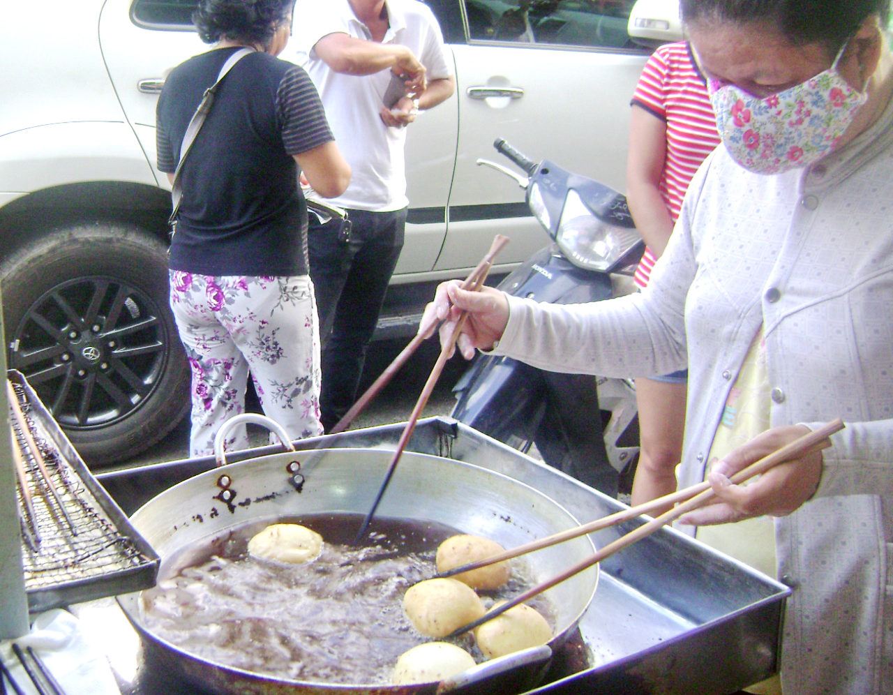 Chiên bánh tiêu trong chảo dầu sôi bằng hai đôi đũa tre dài, cùng lúc dùng cả hai tay, thoăn thoắt liên tục lật bánh cho tới khi chín vàng. (Hình: Văn Lang/Người Việt)