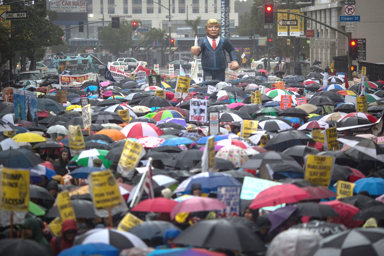 People march in the rain to protest the inauguration of President Donald Trump on January 20, 2017 in Los Angeles,California. / AFP / DAVID MCNEW (Photo credit should read DAVID MCNEW/AFP/Getty Images)