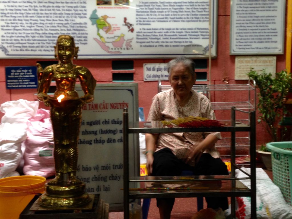 Cụ bà người gốc Ấn ngồi giữ đèn cho khách hành hương thắp hương trong đền bà Mariamman. (Hình: Trần Tiến Dũng/Người Việt)