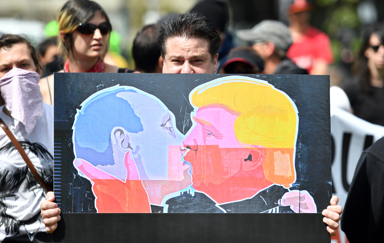 A man holds up a sign showing President Donald Trump kissing Russian President Vladimir Putin at a rally where Trump supporters and anti-Trump protesters clashed in Berkeley, California on April 15, 2017. Hundreds of people with opposing opinions on President Donald Trump threw stones, lit fires, tossed explosives and tear gas and attacked each other with makeshift weapons as police stood by. / AFP PHOTO / Josh Edelson (Photo credit should read JOSH EDELSON/AFP/Getty Images)