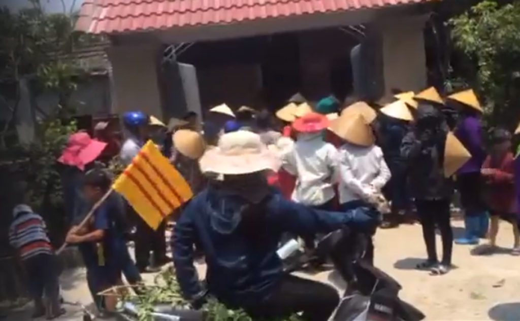 Dân vây nhà chủ tịch xã Kỳ Hà ngày 9 Tháng Tư với cờ VNCH. (Hình: Cắt từ clip)