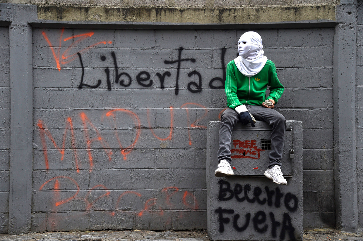 TOPSHOT - A Venezuelan opposition activist sits against a wall reading "Freedom!" during a protest against President Nicolas Maduro, in Caracas on May 8, 2017. Venezuela's opposition mobilized Monday in fresh street protests against President Nicolas Maduro's efforts to reform the constitution in a deadly political crisis. Supporters of the opposition Democratic Unity Roundtable (MUD) gathered in eastern Caracas to march to the education ministry under the slogan "No to the dictatorship." / AFP PHOTO / JUAN BARRETO (Photo credit should read JUAN BARRETO/AFP/Getty Images)