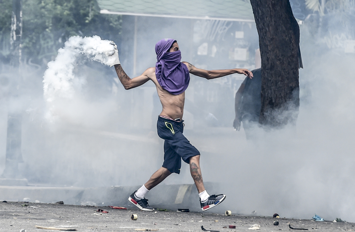An opposition activist hurls back at riot police a tear gas canister during clashes ensuing a protest against President Nicolas Maduro, in Caracas on May 8, 2017. Venezuela's opposition mobilized Monday in fresh street protests against President Nicolas Maduro's efforts to reform the constitution in a deadly political crisis. Supporters of the opposition Democratic Unity Roundtable (MUD) gathered in eastern Caracas to march to the education ministry under the slogan "No to the dictatorship." / AFP PHOTO / JUAN BARRETO (Photo credit should read JUAN BARRETO/AFP/Getty Images)