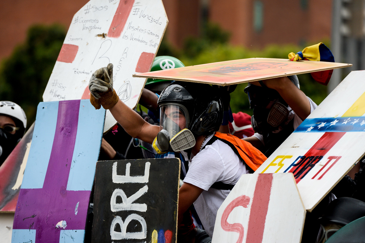Opposition demonstrators wearing helmets, protective gloves and gas masks take cover behind makeshift shields as they clash with riot police during a protest against President Nicolas Maduro, in Caracas on May 8, 2017. Venezuela's opposition mobilized Monday in fresh street protests against President Nicolas Maduro's efforts to reform the constitution in a deadly political crisis. Supporters of the opposition Democratic Unity Roundtable (MUD) gathered in eastern Caracas to march to the education ministry under the slogan "No to the dictatorship." / AFP PHOTO / FEDERICO PARRA (Photo credit should read FEDERICO PARRA/AFP/Getty Images)
