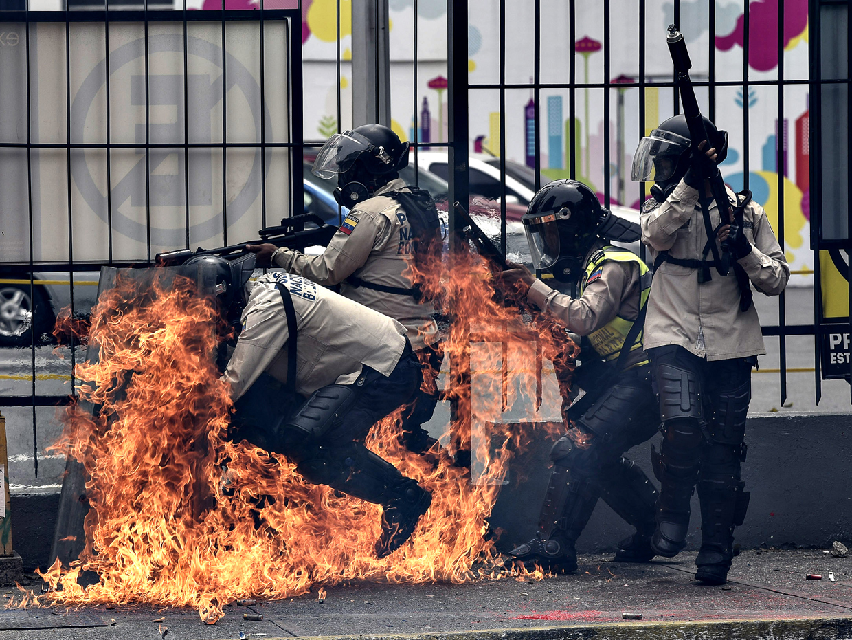TOPSHOT - A group of riot policemen are hit by a Molotov cocktail hurled by an opposition demonstrator during a protest against President Nicolas Maduro, in Caracas on May 8, 2017. Venezuela's opposition mobilized Monday in fresh street protests against President Nicolas Maduro's efforts to reform the constitution in a deadly political crisis. Supporters of the opposition Democratic Unity Roundtable (MUD) gathered in eastern Caracas to march to the education ministry under the slogan "No to the dictatorship." / AFP PHOTO / CARLOS BECERRA (Photo credit should read CARLOS BECERRA/AFP/Getty Images)
